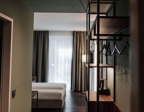 Modern hotel room with neatly made bed, open closet and large window with sheer curtains.