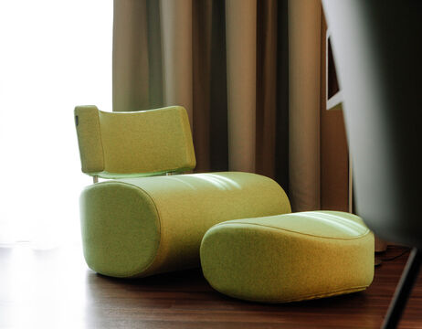 Hellgrüner moderner Loungesessel mit passender Ottomane auf einem Holzboden, in der Nähe von Vorhängen und weichem Tageslicht.