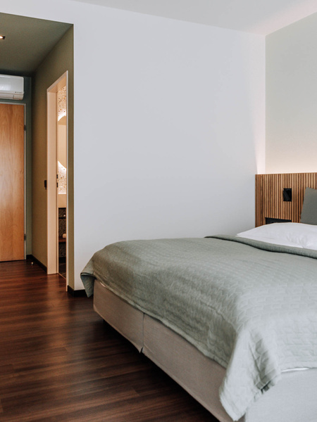 Modern hotel room with neatly made bed, wooden floor, desk and door to the bathroom.
