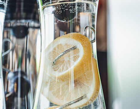 Nahaufnahme von Zitronenscheiben in sprudelndem Wasser in einem Glaskrug, mit sichtbaren Blasen.