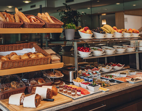 Frühstücksbuffet mit Körben mit Brot, Gebäck, frischem Obst und verschiedenen Gerichten auf einer Theke.