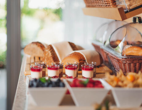 Frühstücksbuffet mit verschiedenen Brotsorten, Gebäck, Joghurtparfaits und Schalen mit frischen Beeren auf einer Theke.