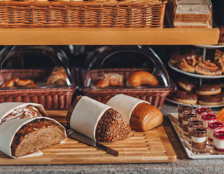 Drei Brote auf einem Schneidebrett, Gebäck in Körben und verschiedene Desserts auf einer Theke.