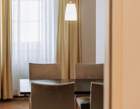Dining table with four gray chairs, white curtains and a hanging lamp in a softly lit room.
