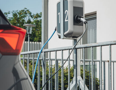 Nahaufnahme eines Elektroautos, das an einer mit 1 und 2 gekennzeichneten Ladestation im Freien in der Nähe eines Gebäudes aufgeladen wird.