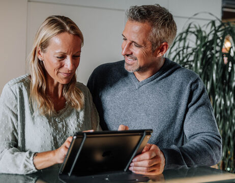Ein lächelndes Paar sitzt zusammen und schaut auf eine Tafel auf einem Tisch in einem Haus.