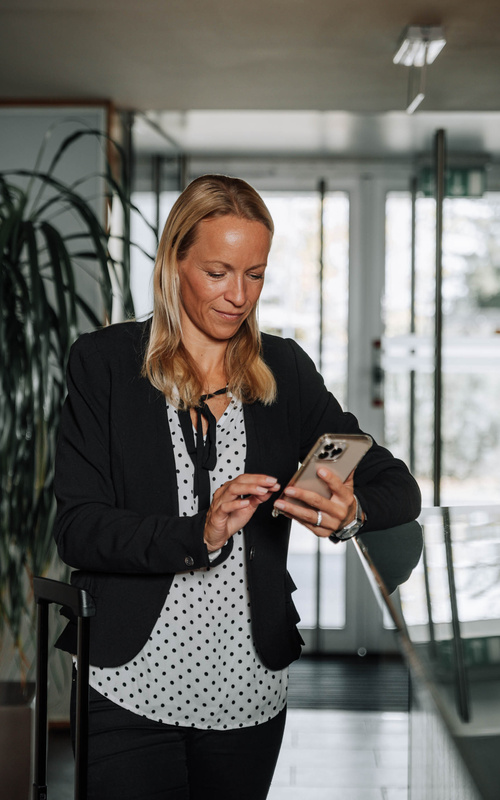 Woman in a black blazer using her smartphone in a modern interior.
