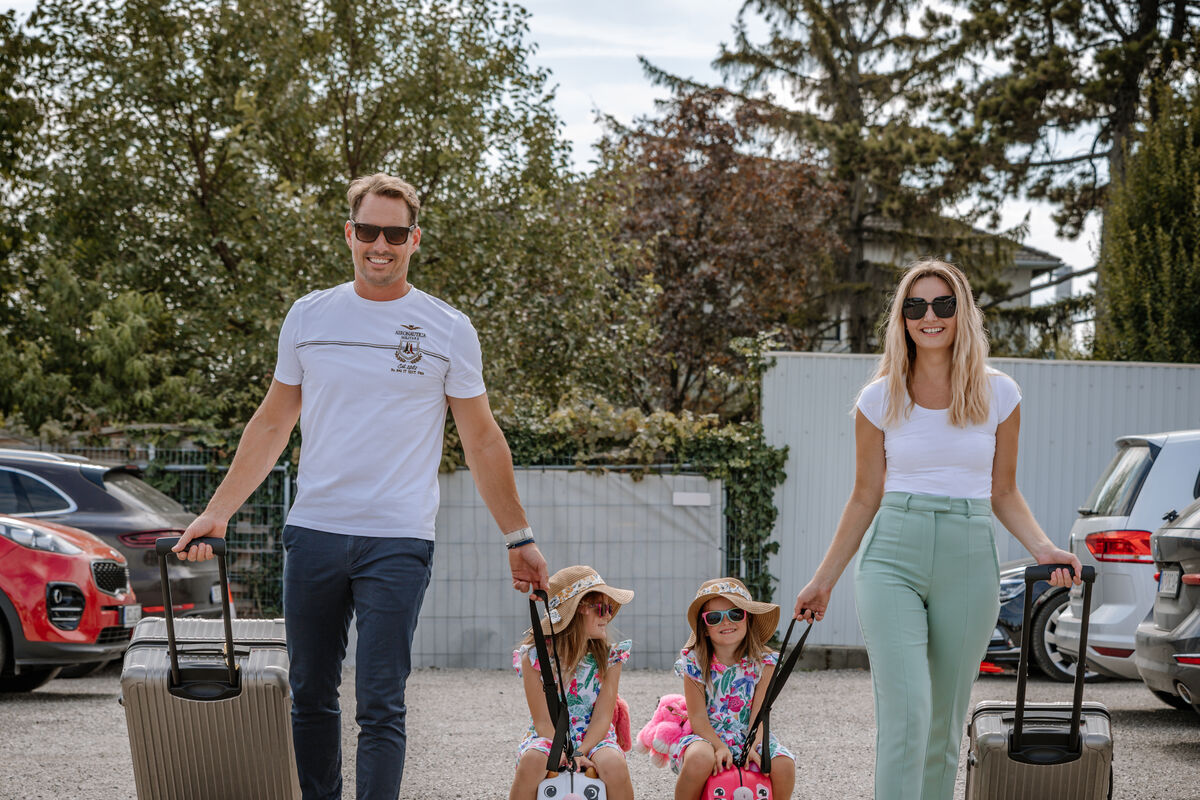 Eine lächelnde vierköpfige Familie mit Koffern steht an einem sonnigen Tag im Freien, bereit für die Reise.