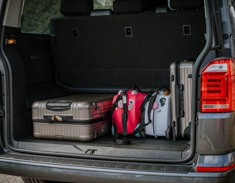 Drei Koffer, darunter zwei Metallkoffer und eine rosa Kindertasche, im offenen Kofferraum eines Autos.