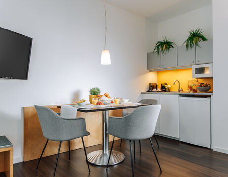 Moderne Küchenzeile mit kleinem Esstisch, grauen Stühlen und Topfpflanzen bei warmer Beleuchtung.