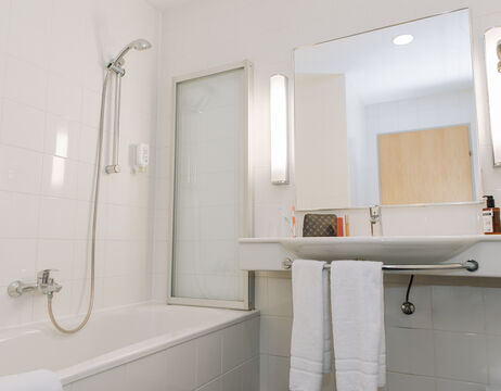 Ein weißes Badezimmer mit einer Badewanne, einer Dusche, einem Waschbecken, einem Spiegel und zwei weißen Handtüchern, die über dem Waschbecken hängen.