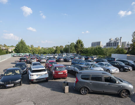 Dicht an dicht geparkte Autos auf einem überfüllten Parkplatz unter einem teilweise bewölkten Himmel.
