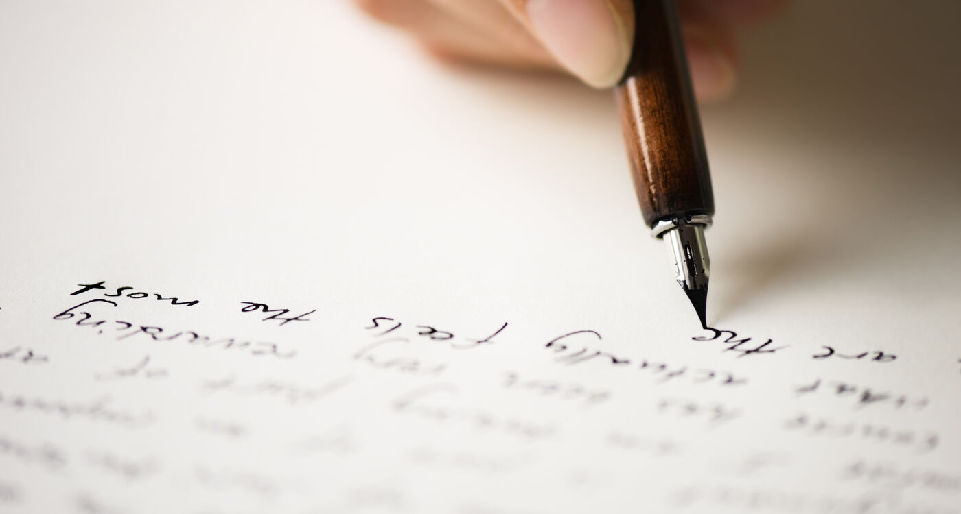 Eine Hand, die mit einem Füllfederhalter auf weißem Papier schreibt, das mit kursiver Handschrift gefüllt ist.